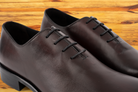 Pair of burgundy Italian wholecut Oxford shoe with laces on a wooden surface.