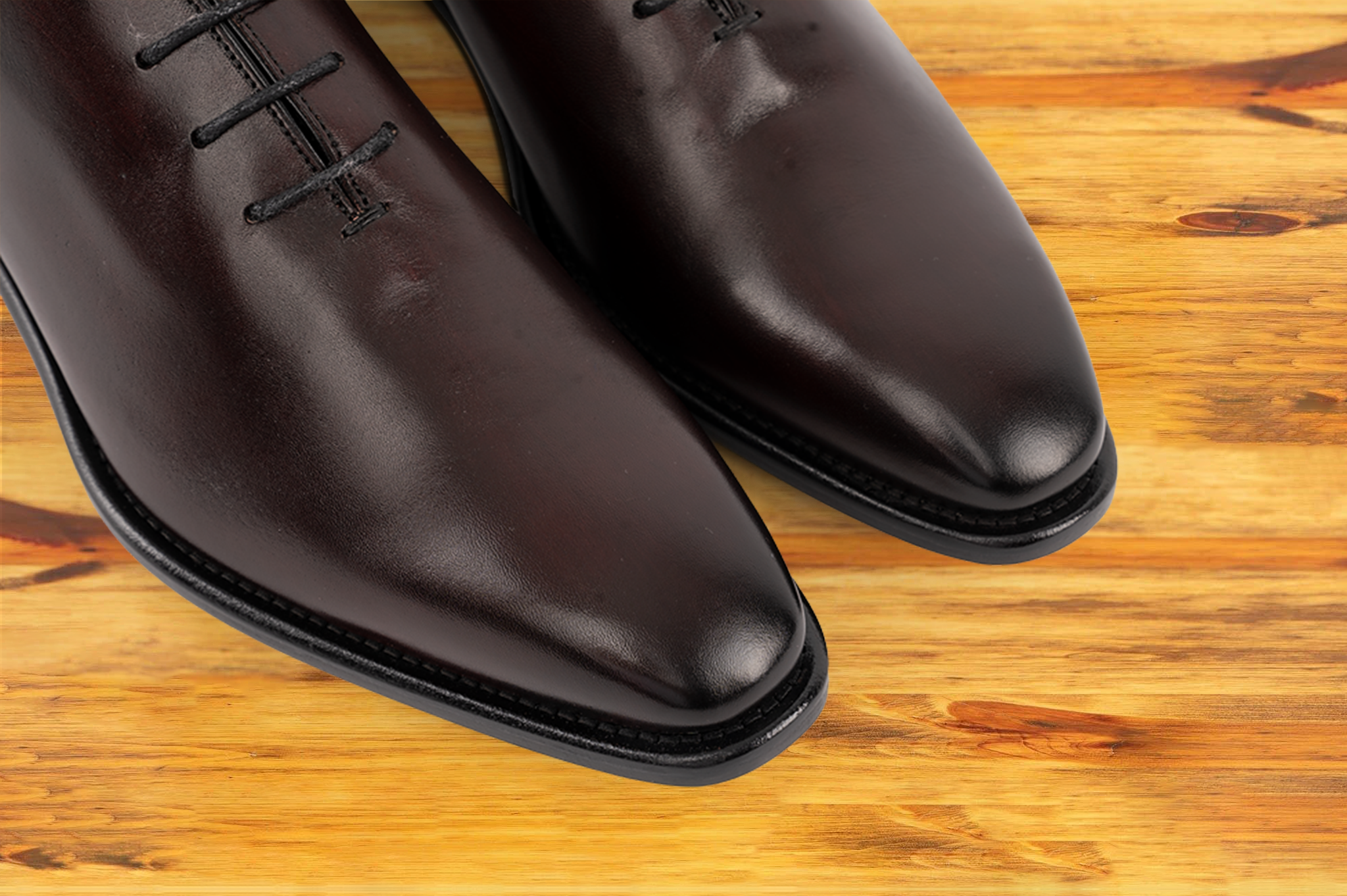 Pair of burgundy Italian wholecut Oxford shoe with laces on a wooden surface.