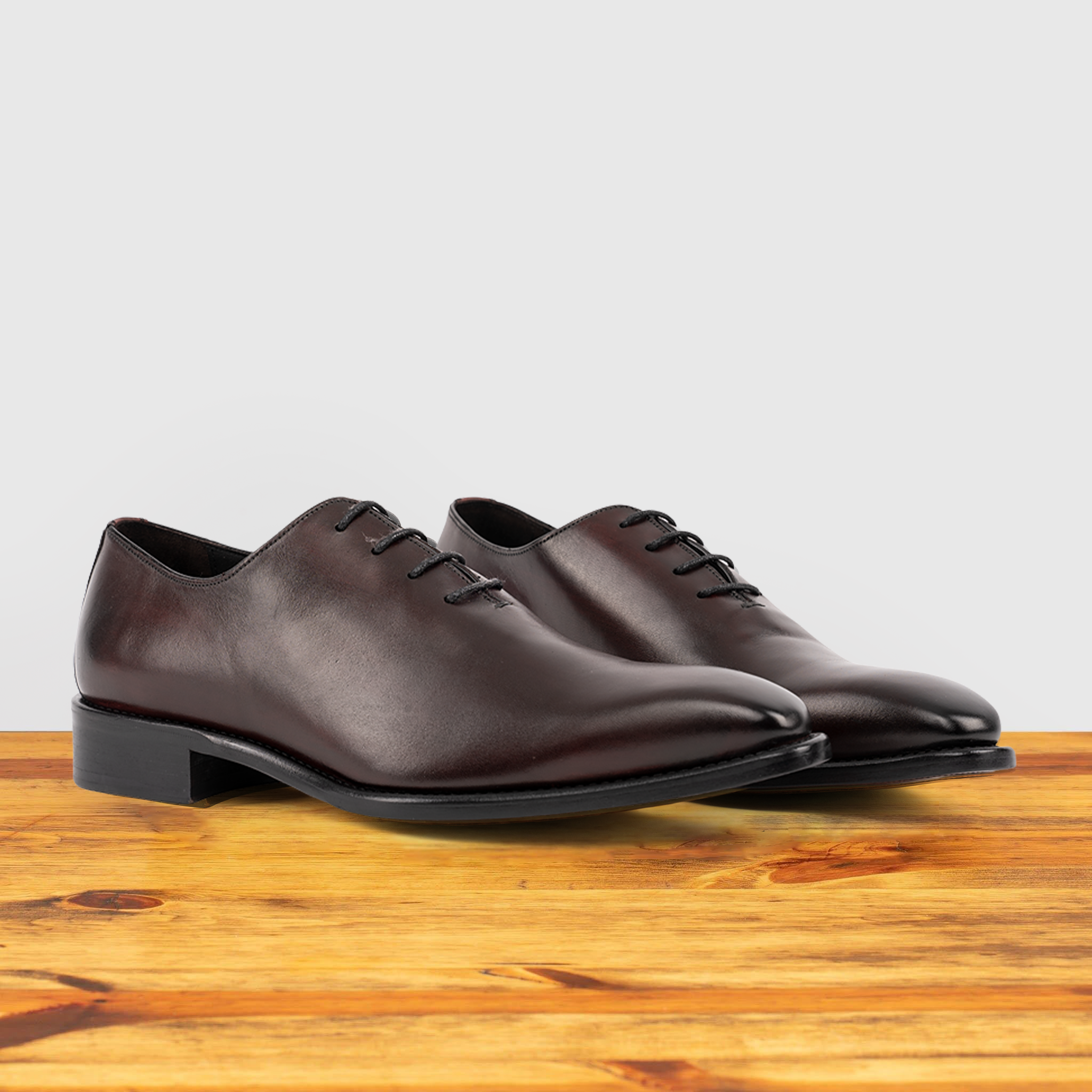 Pair of burgundy Italian wholecut Oxford shoe with laces on a wooden surface.