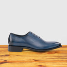 Blue leather dress shoe on a wooden surface with a light gray background
