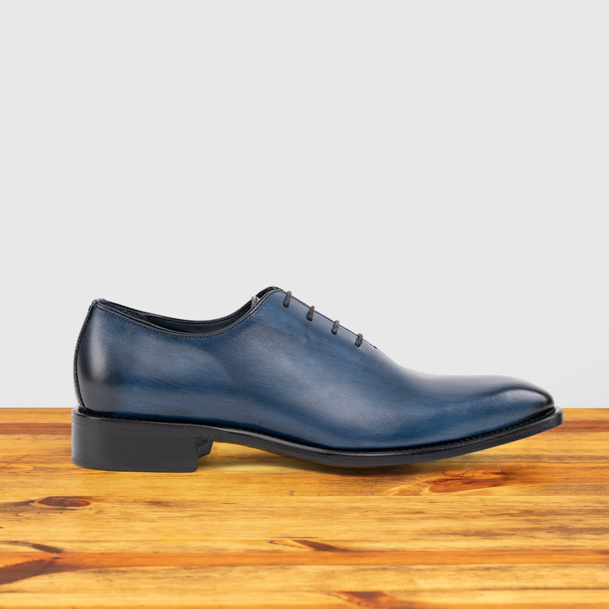 Blue leather dress shoe on a wooden surface with a light gray background