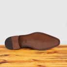Outsole of Blue leather dress shoe on a wooden surface with a light gray background