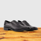 A Pair of Graphite Italian wholecut Oxford shoe with laces on a wooden surface.