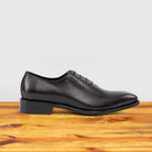 A single Graphite Italian wholecut Oxford shoe with laces on a wooden surface.
