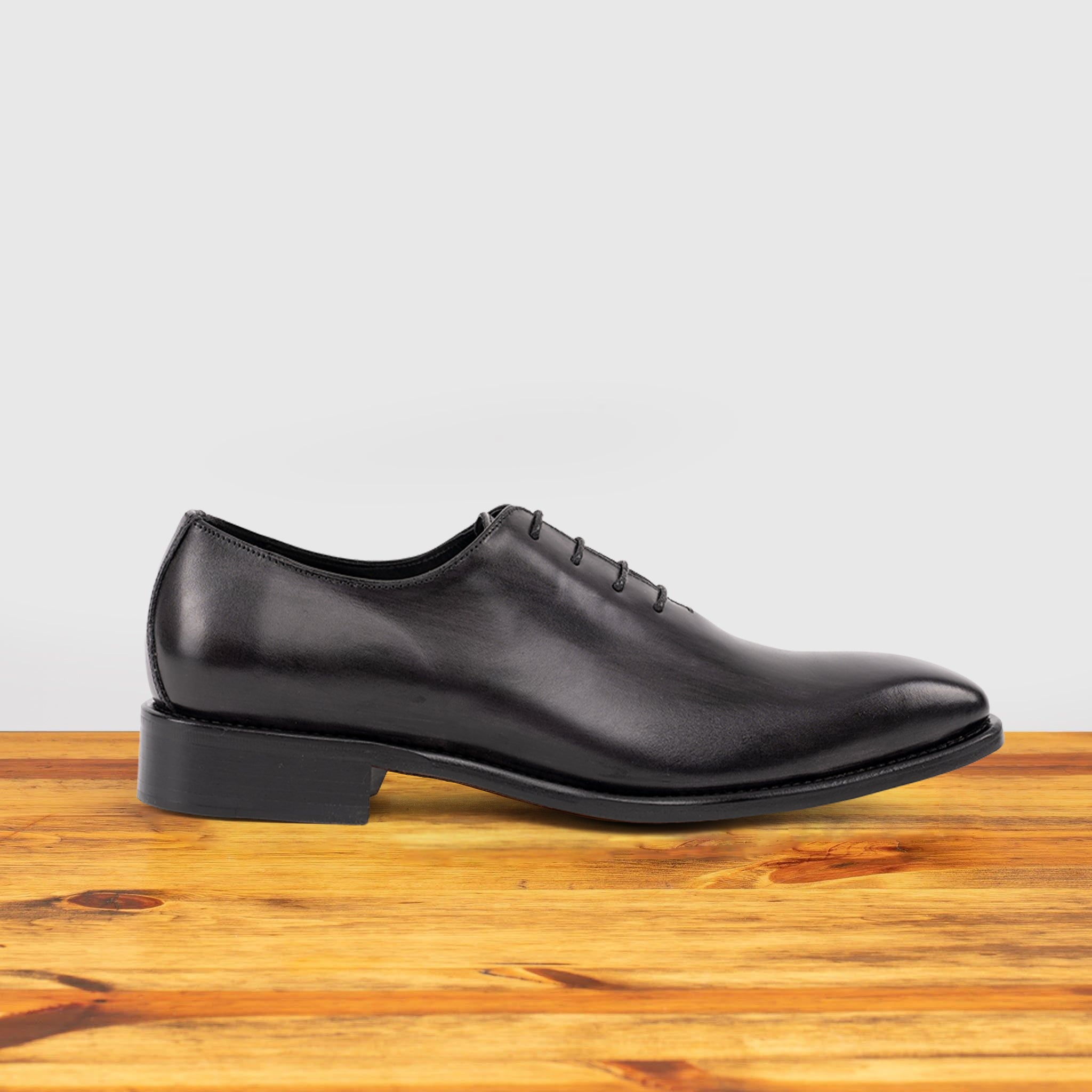 A single Graphite Italian wholecut Oxford shoe with laces on a wooden surface.