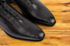 A Pair of Graphite Italian wholecut Oxford shoe with laces on a wooden surface.