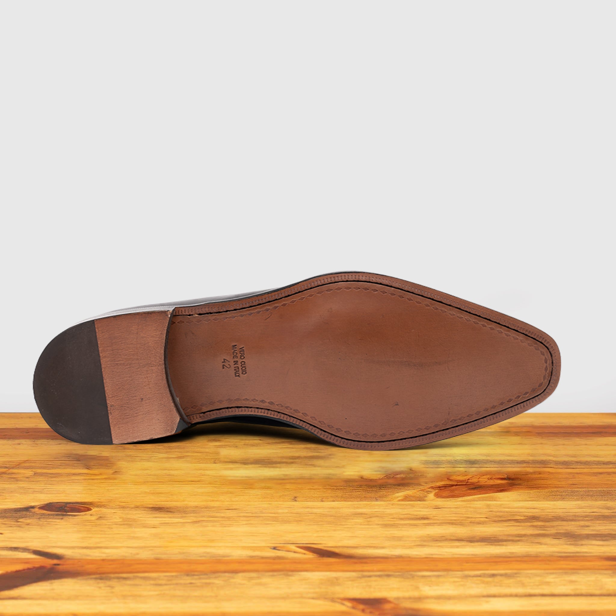 Outsole of Graphite Italian wholecut Oxford shoe with laces on a wooden surface.