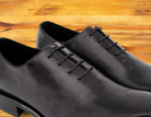 A Pair of Graphite Italian wholecut Oxford shoe with laces on a wooden surface.