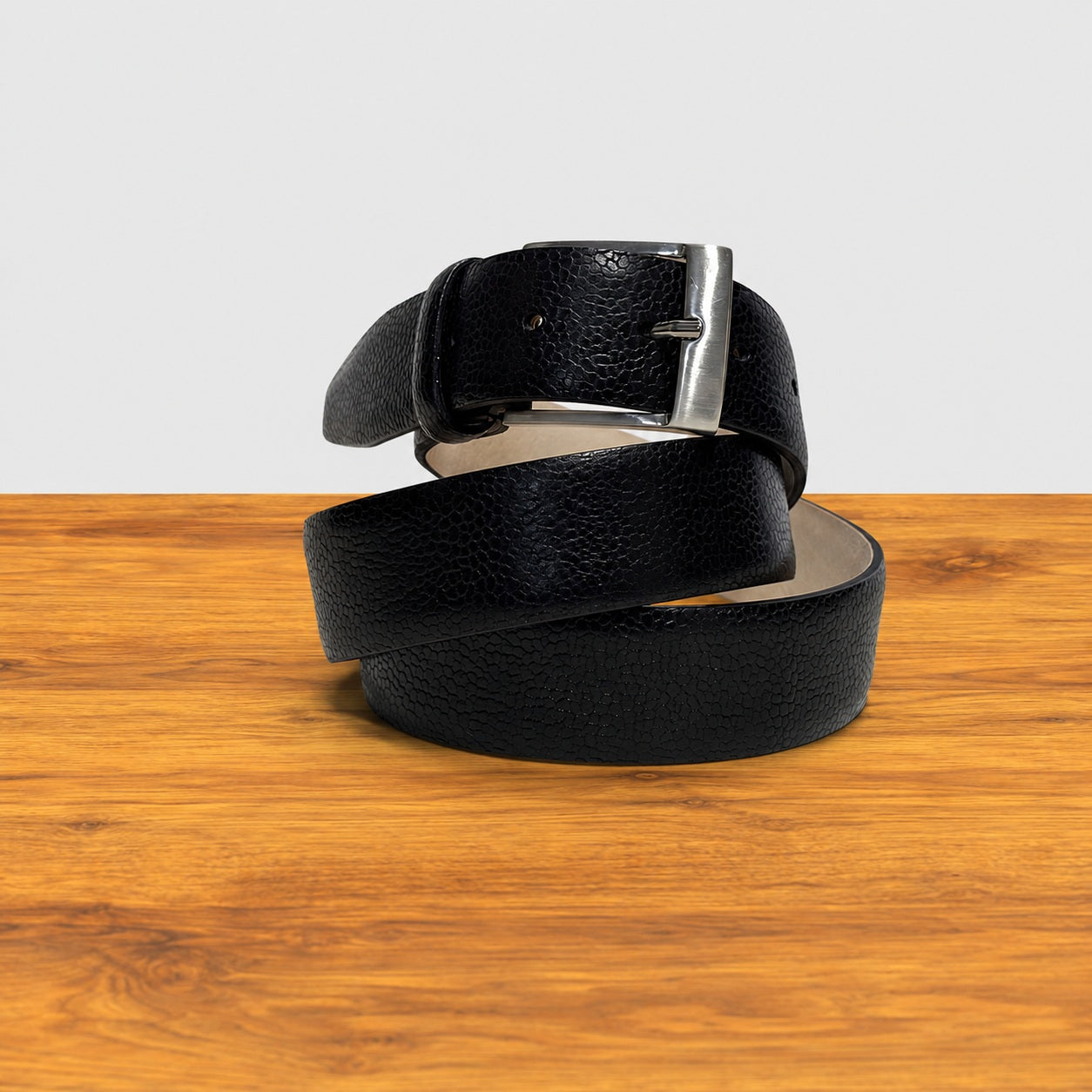 Black leather belt with silver buckle on a wooden surface
