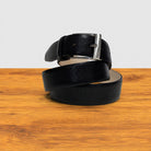 Black leather belt with silver buckle on a wooden surface