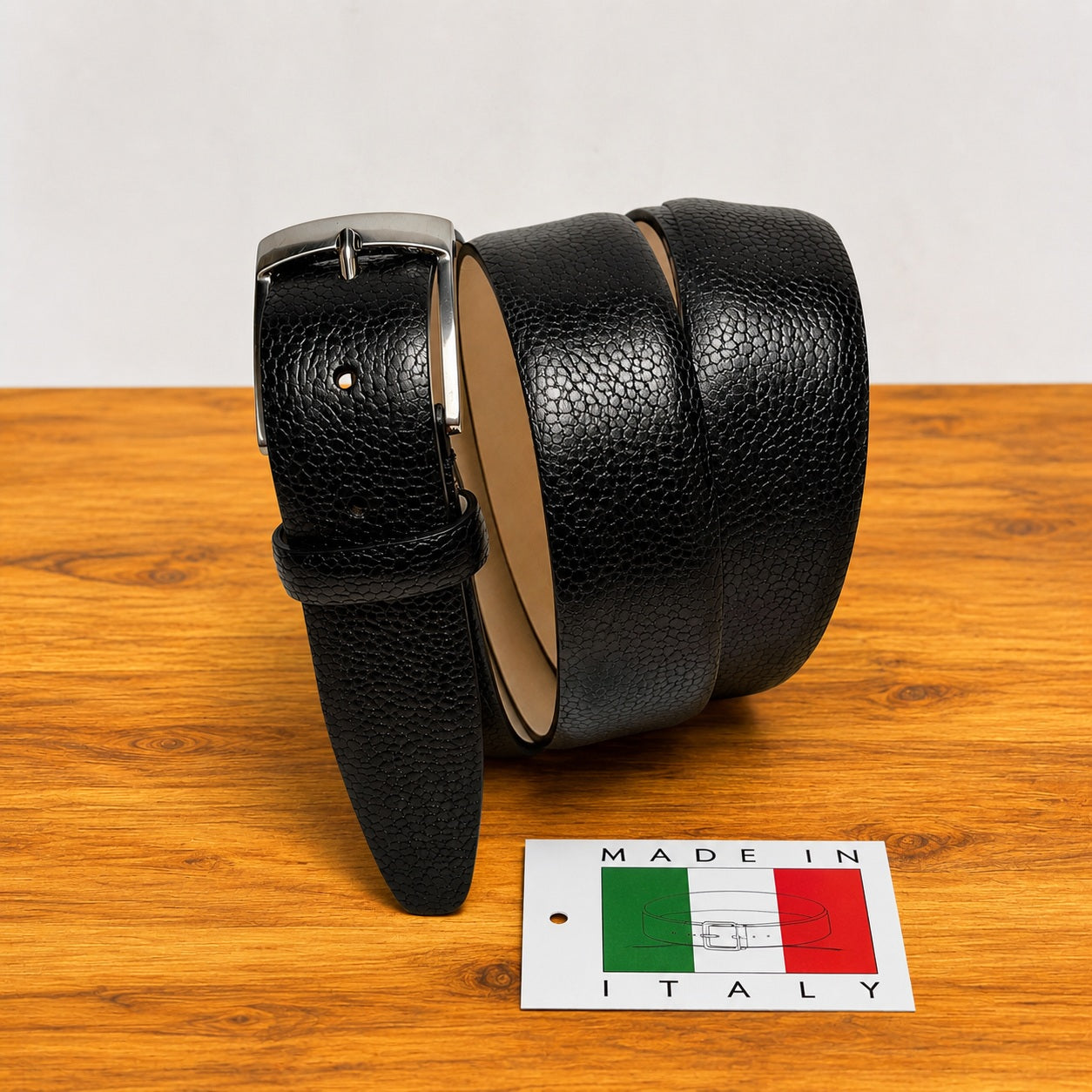 Black leather belt on a wooden surface with a 'Made in Italy' sign.