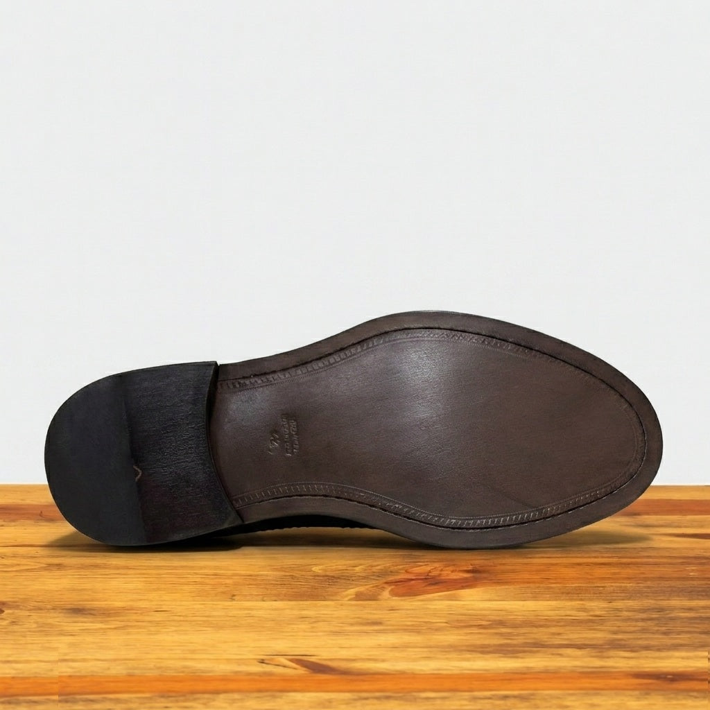 Close-up of a shoe sole, displayed on a rustic wooden surface against a light grey background