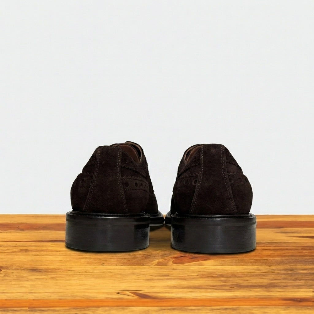 Backside of Chocolate brown suede wingtip shoe displayed on a wooden surface