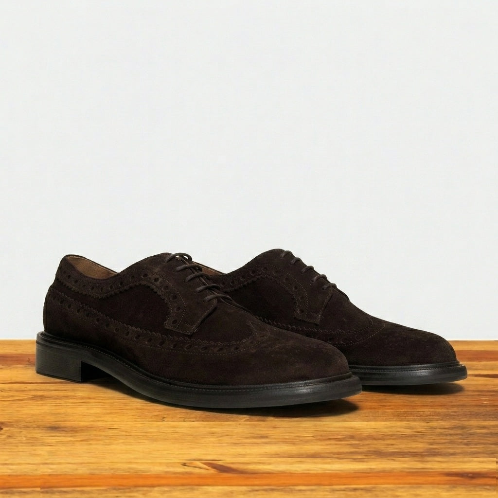 Side view of Chocolate brown suede wingtip shoe with decorative perforations and lace-up closure, displayed on a wooden surface