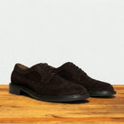 Side view of Chocolate brown suede wingtip shoe with decorative perforations and lace-up closure, displayed on a wooden surface