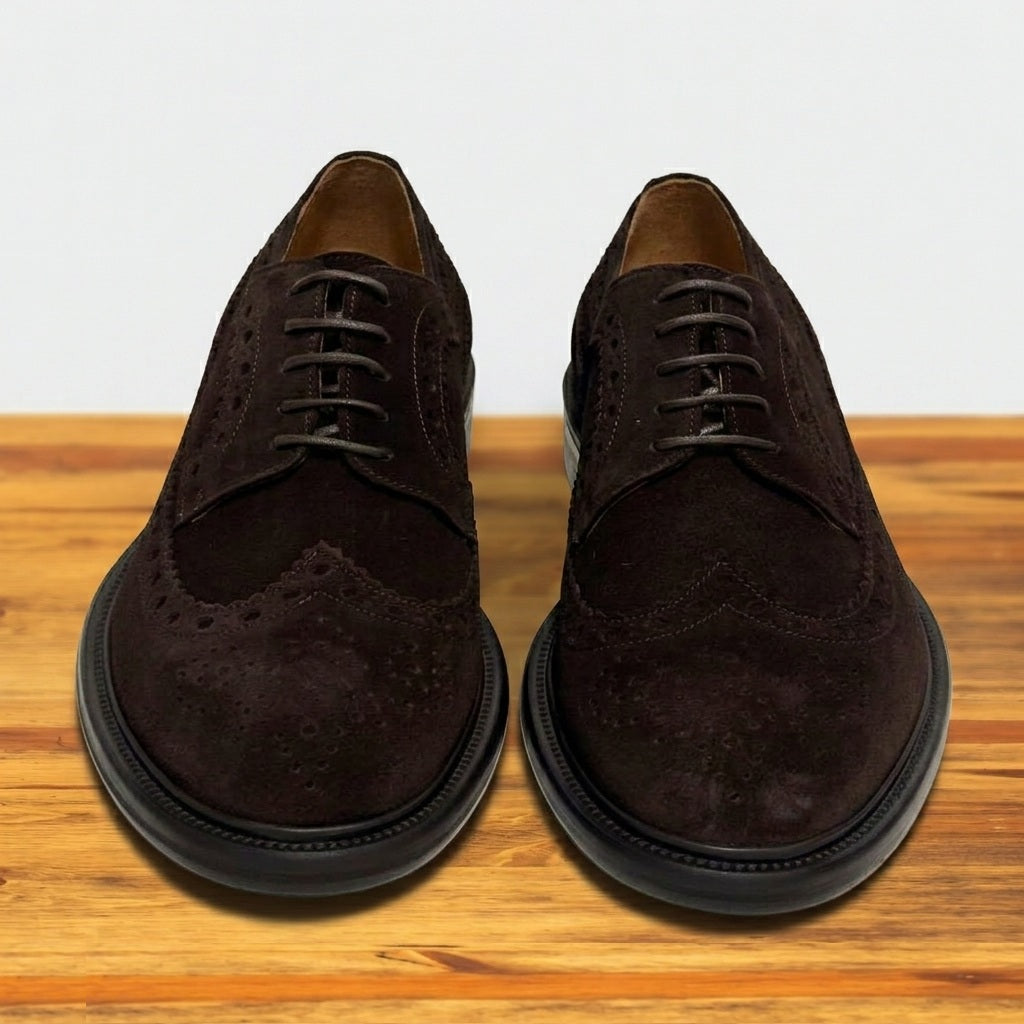 Pair of  Chocolate brown suede wingtip shoe with decorative perforations and lace-up closure, displayed on a wooden surface