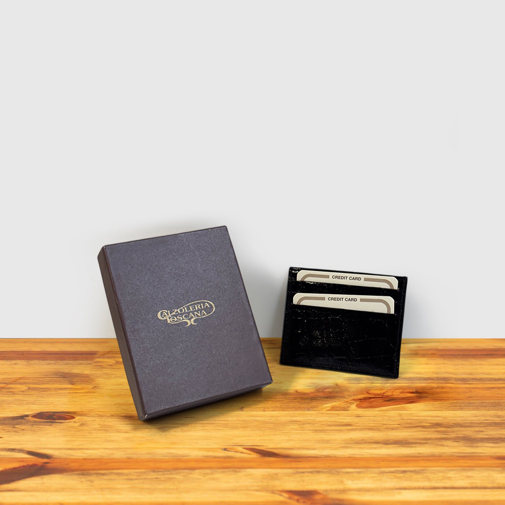 Black crocodile-patterned cardholder with credit cards and box on a wooden surface and light gray background