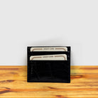 Black crocodile-patterned cardholder with credit cards on a wooden surface and light gray background