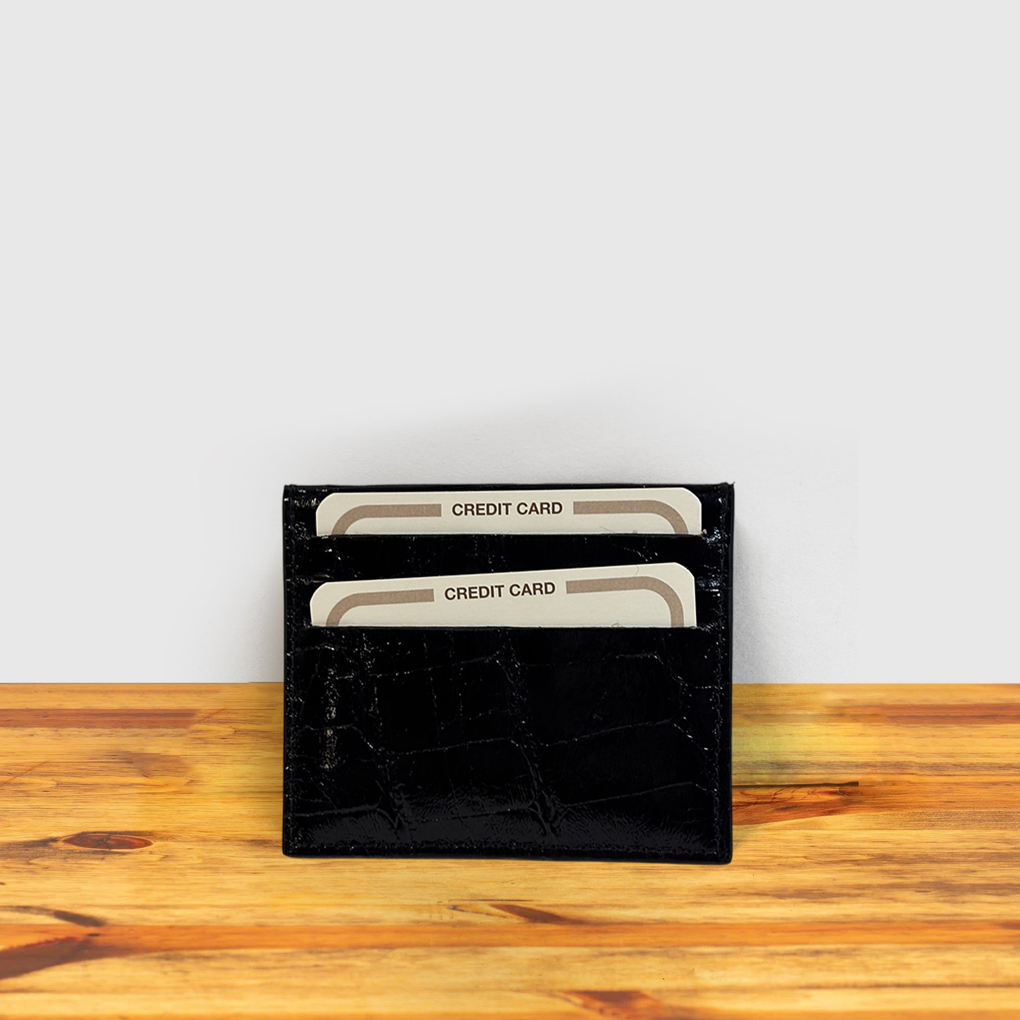 Black crocodile-patterned cardholder with credit cards on a wooden surface and light gray background