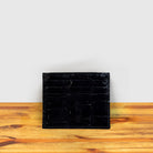 Black Calzoleria Toscana Kang Crocodile Credit Card Holder on a wooden surface and light gray background