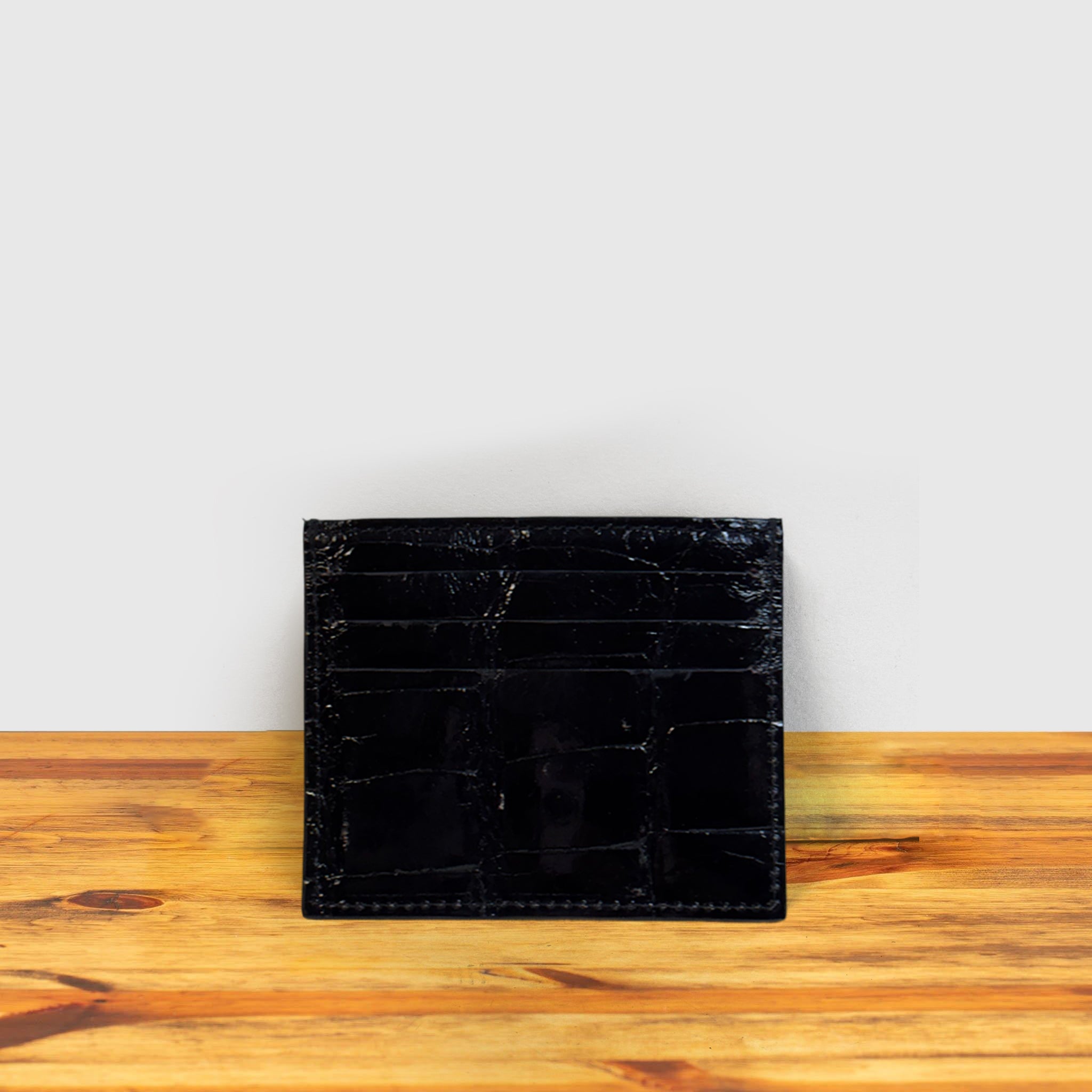 Black Calzoleria Toscana Kang Crocodile Credit Card Holder on a wooden surface and light gray background