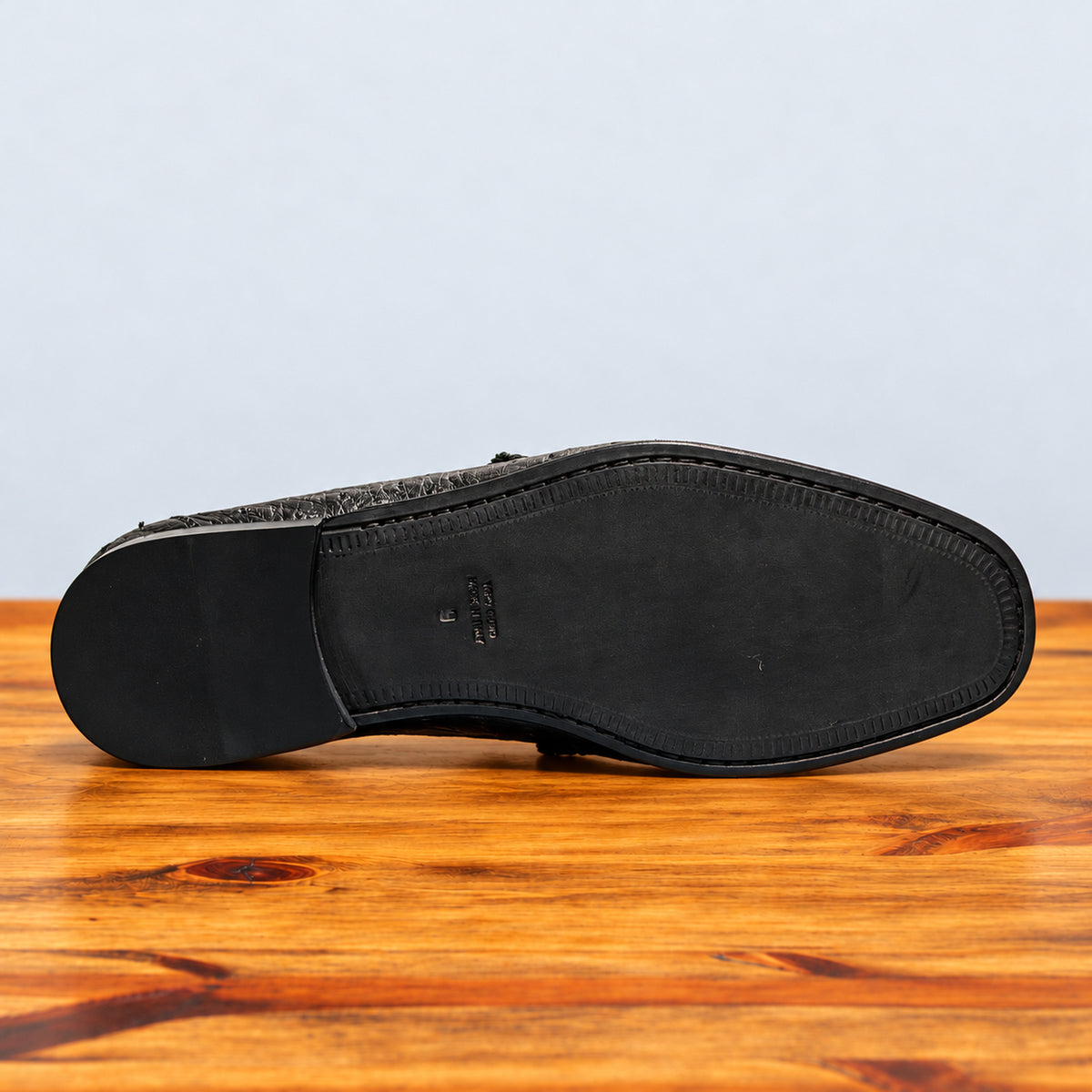 Outsole of Black  Ostrich leather loafer on a wooden surface with a light gray background