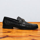 Black ostrich loafer on top of a wooden table showing the side profile of the shoe.
