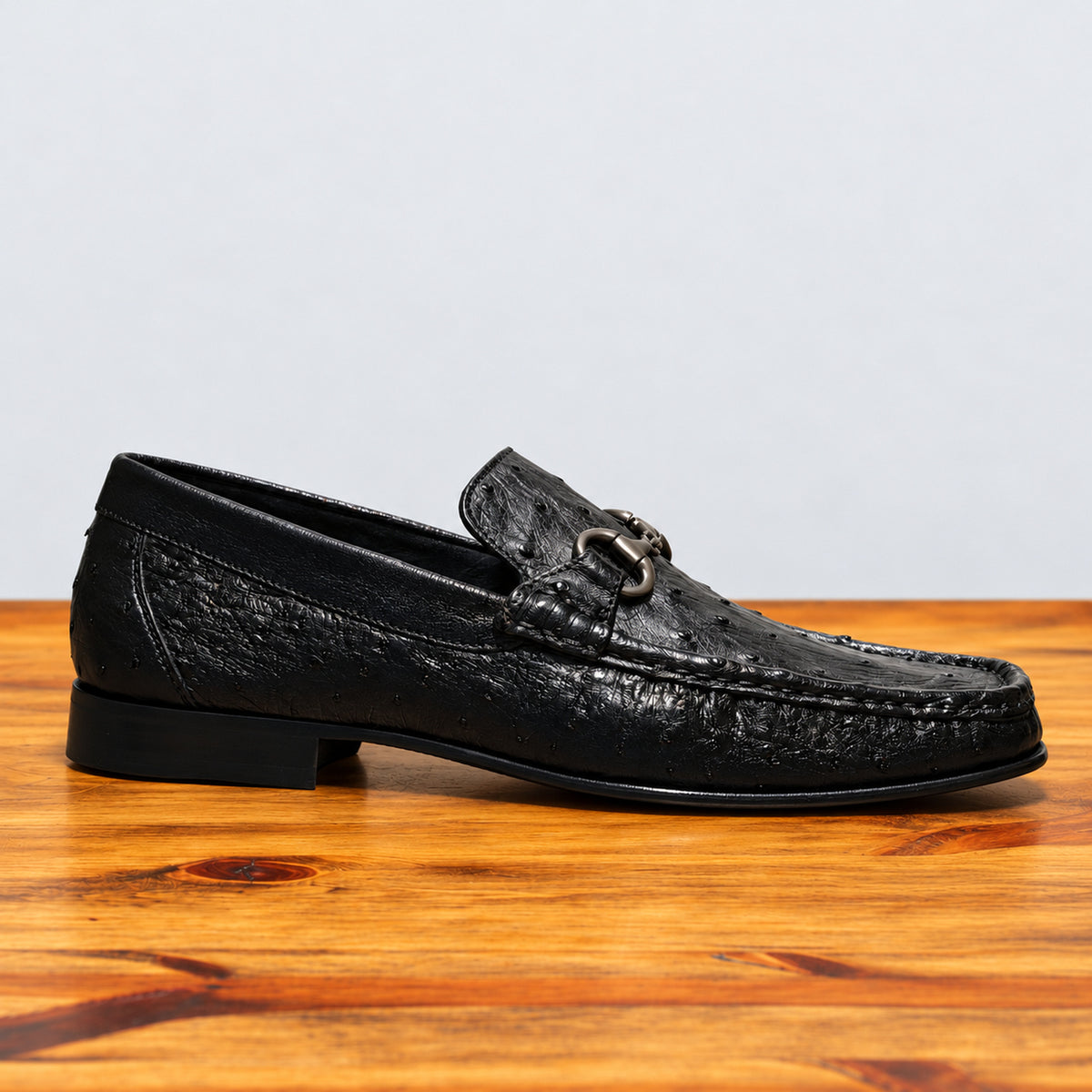 Black ostrich loafer on top of a wooden table showing the side profile of the shoe.
