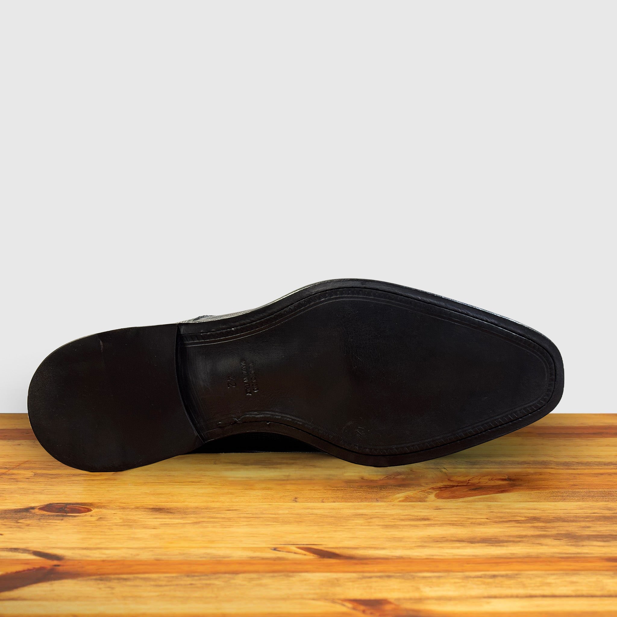 Outsole of Black leather dress shoe on a wooden surface with a light gray background