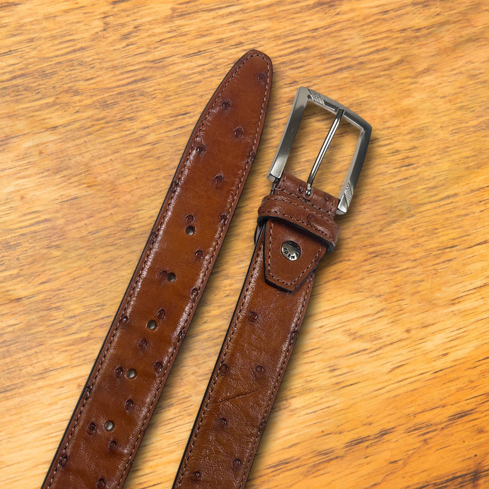 Cognac ostrich-patterned belt on a wooden surface with a white background