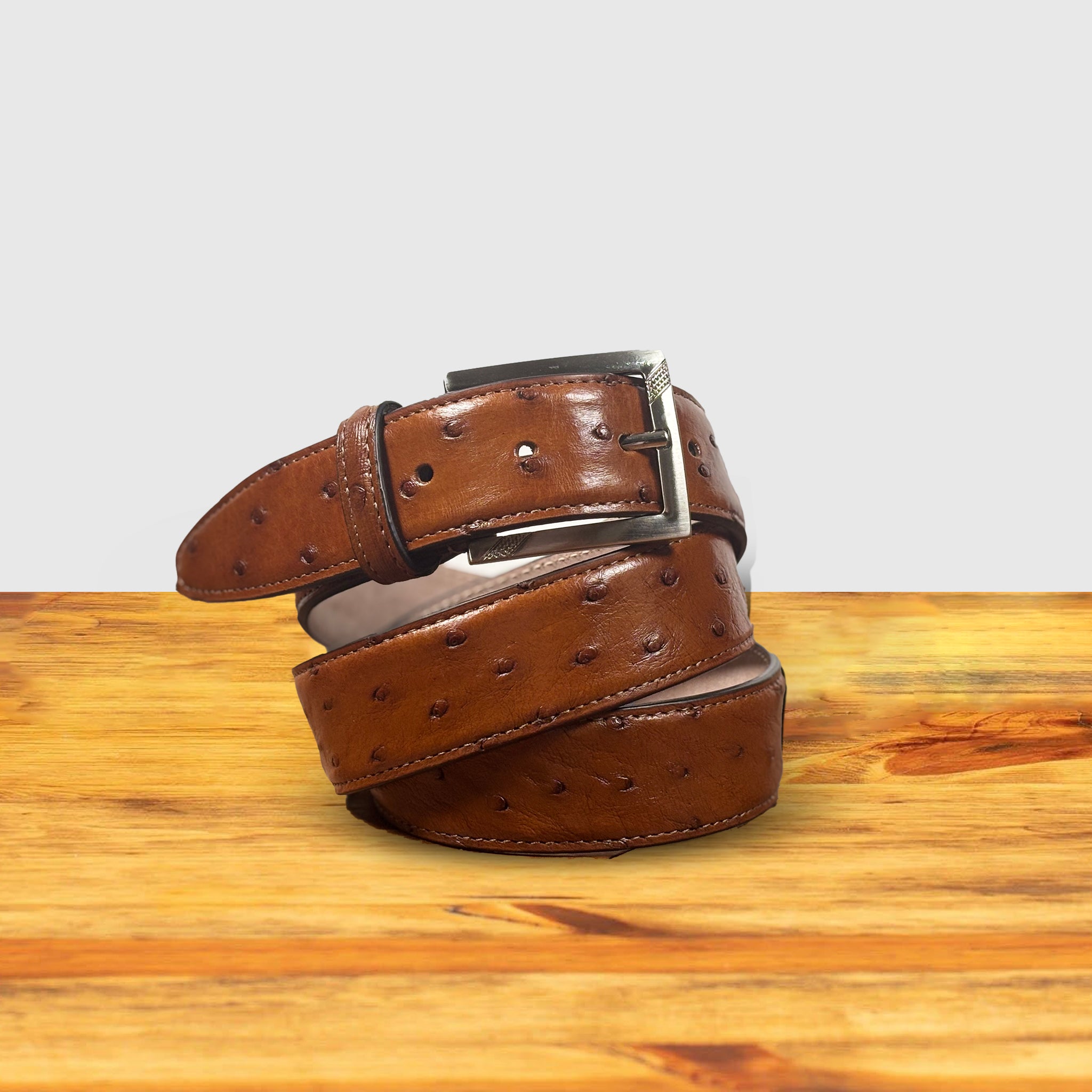 Cognac ostrich-patterned belt on a wooden surface with a white background