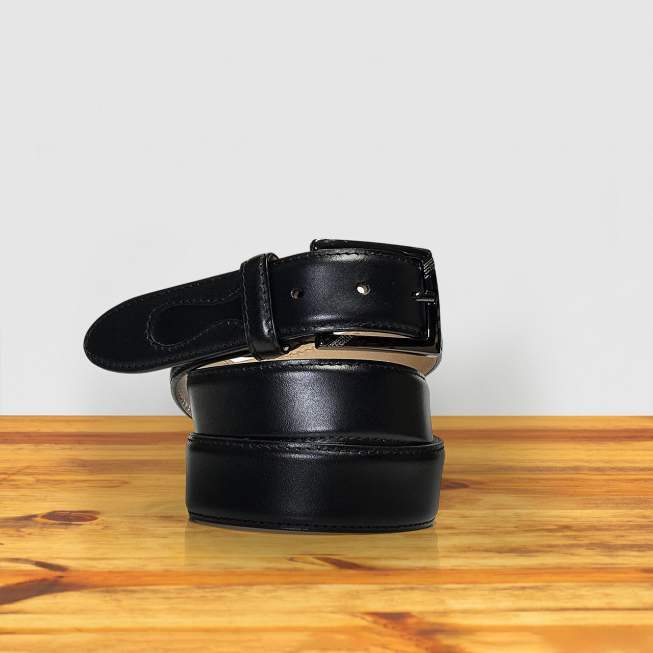 Black leather belt on a wooden surface with a light gray background