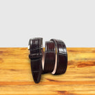 Burgundy leather belt with a silver buckle on a wooden surface