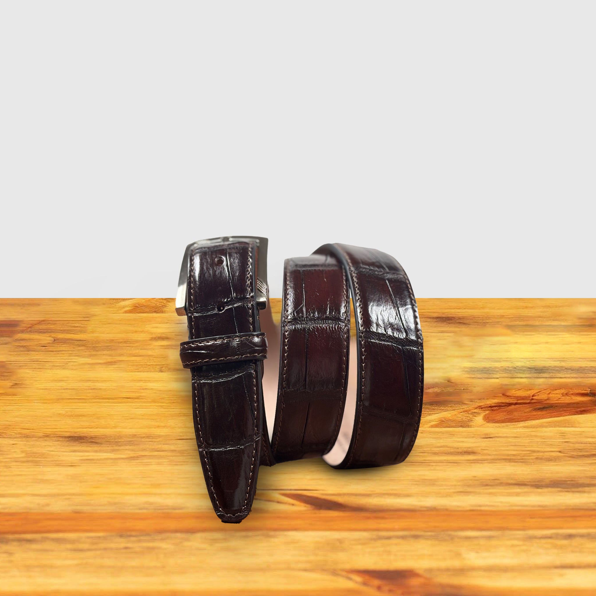 Burgundy leather belt with a silver buckle on a wooden surface