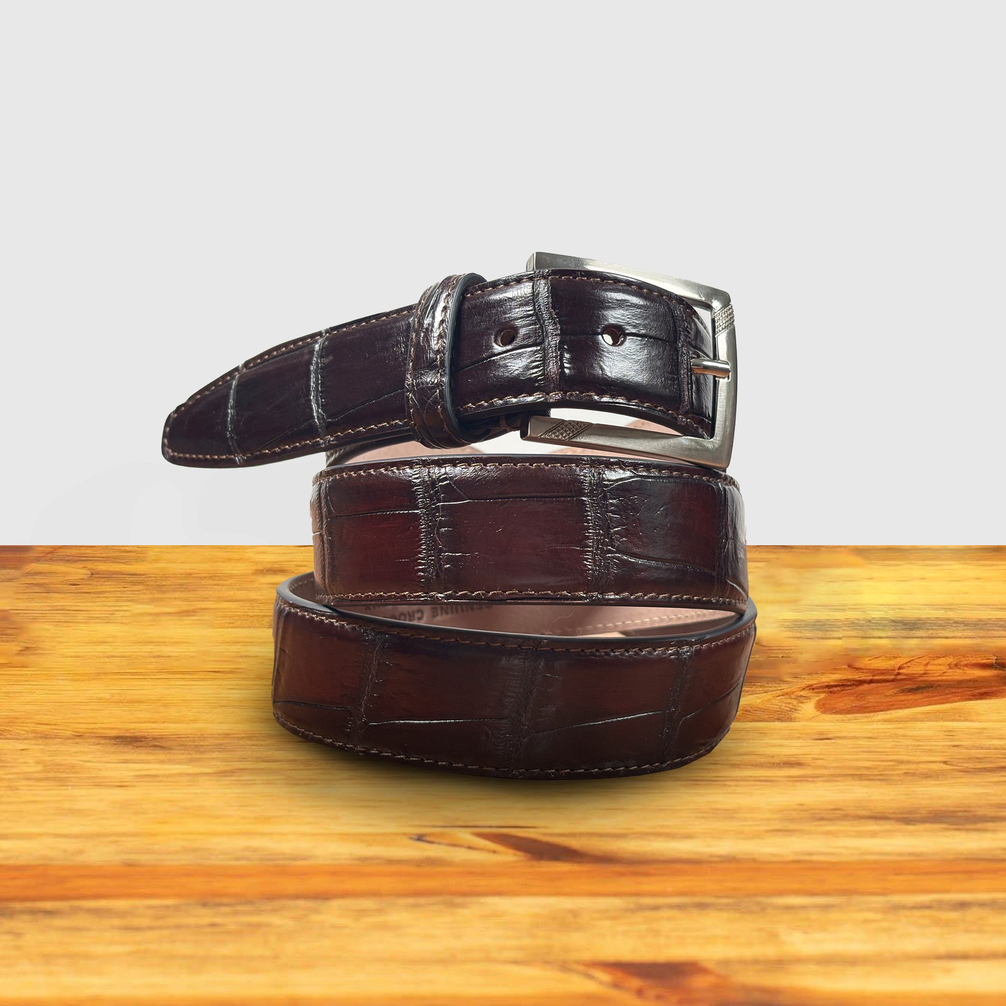 Burgundy leather belt with a silver buckle on a wooden surface