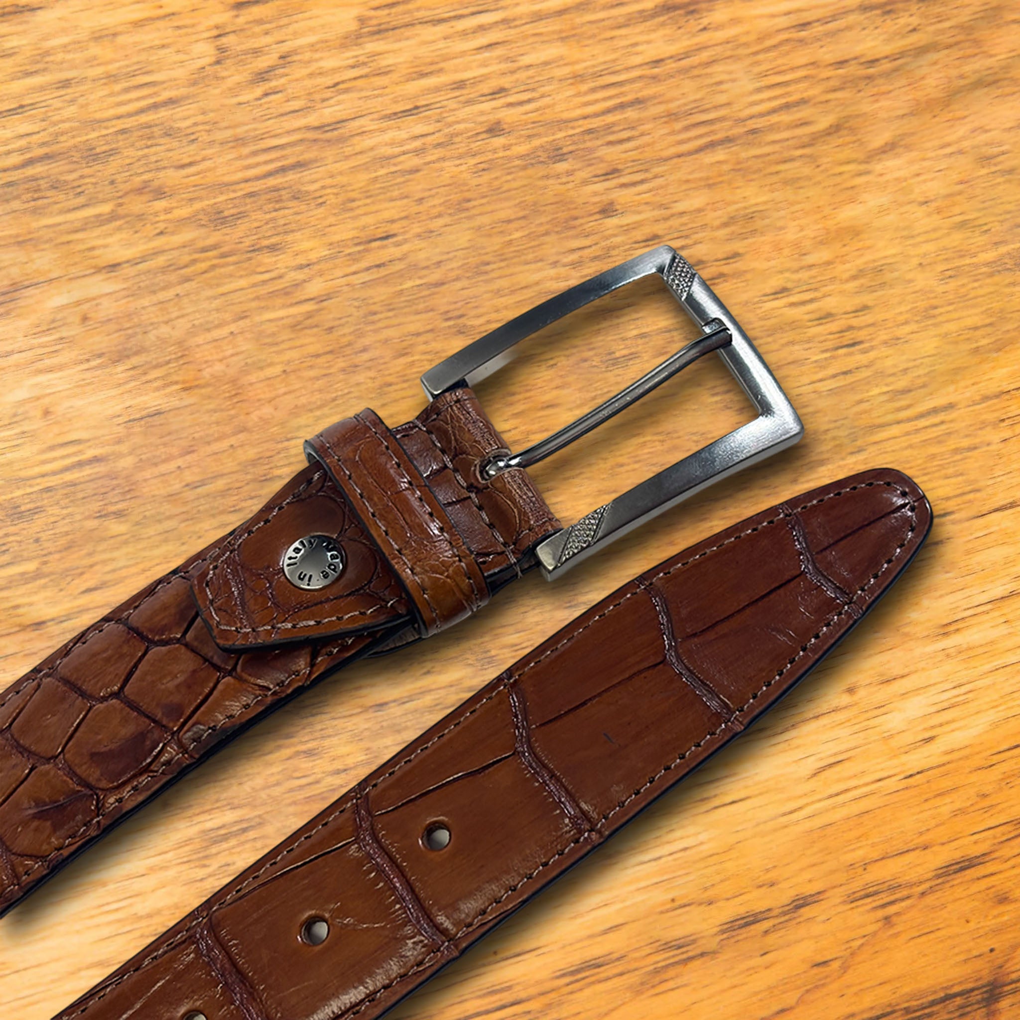 C8099 Cognac Calzoleria Toscana Crocodile Belt on a wooden surface
