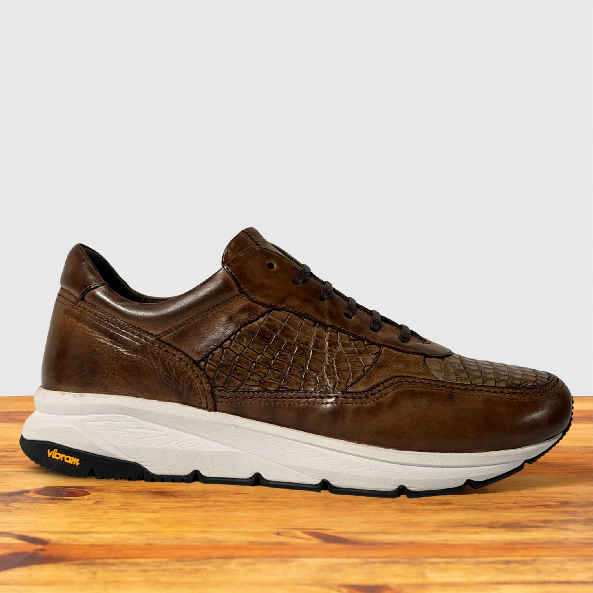 A Moor leather Vibram sneaker with textured overlays and a thick white midsole, displayed on a wooden surface against a light gray background.