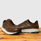 A pair of brown leather athletic sneakers and thick white midsoles, displayed on a wooden surface against a light gray background.