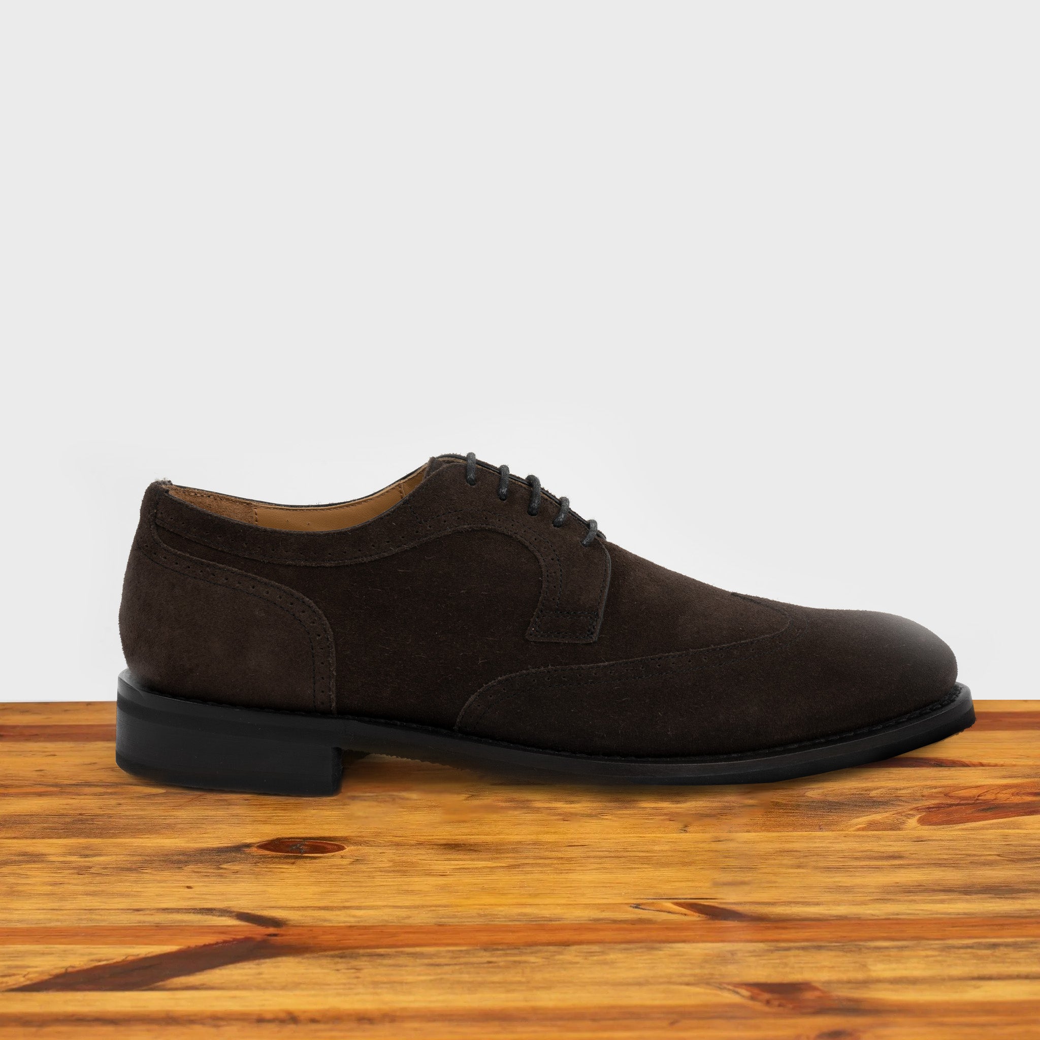 Charcoal suede dress shoe on a wooden surface with a light gray background