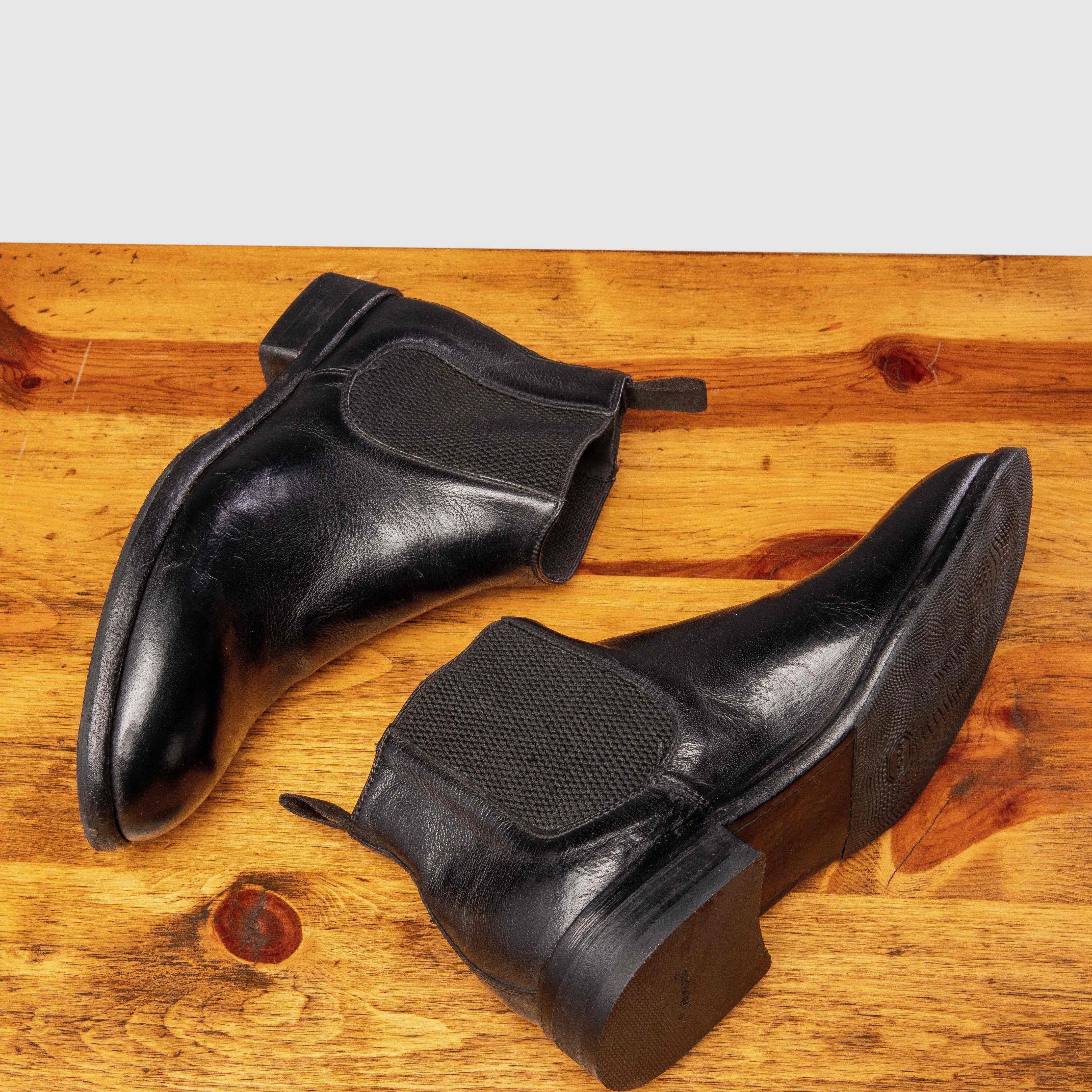 Pair of black leather Chelsea boots on a wooden surface with a light gray background