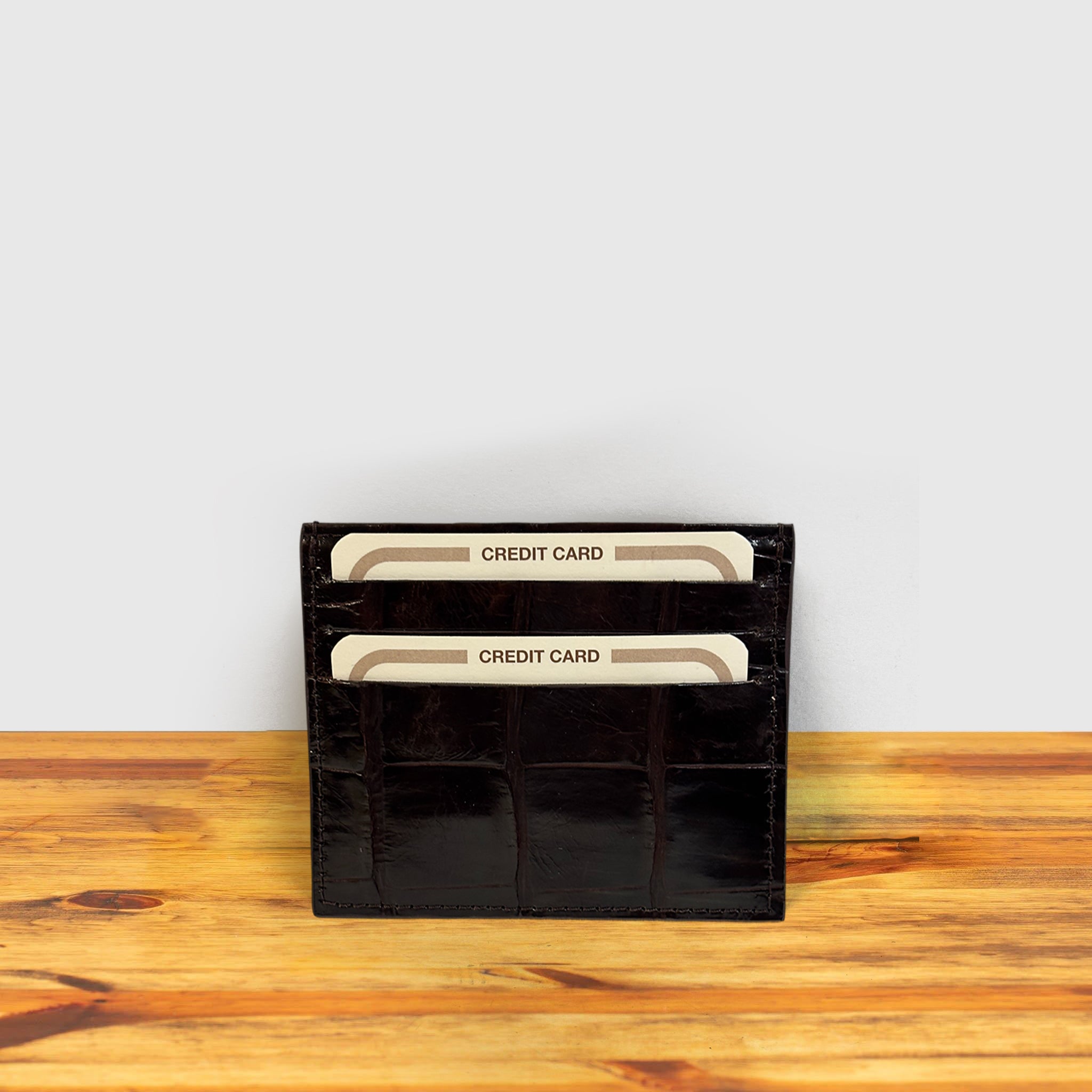 Dark Brown crocodile-patterned cardholder with credit cards on a wooden surface and light gray background