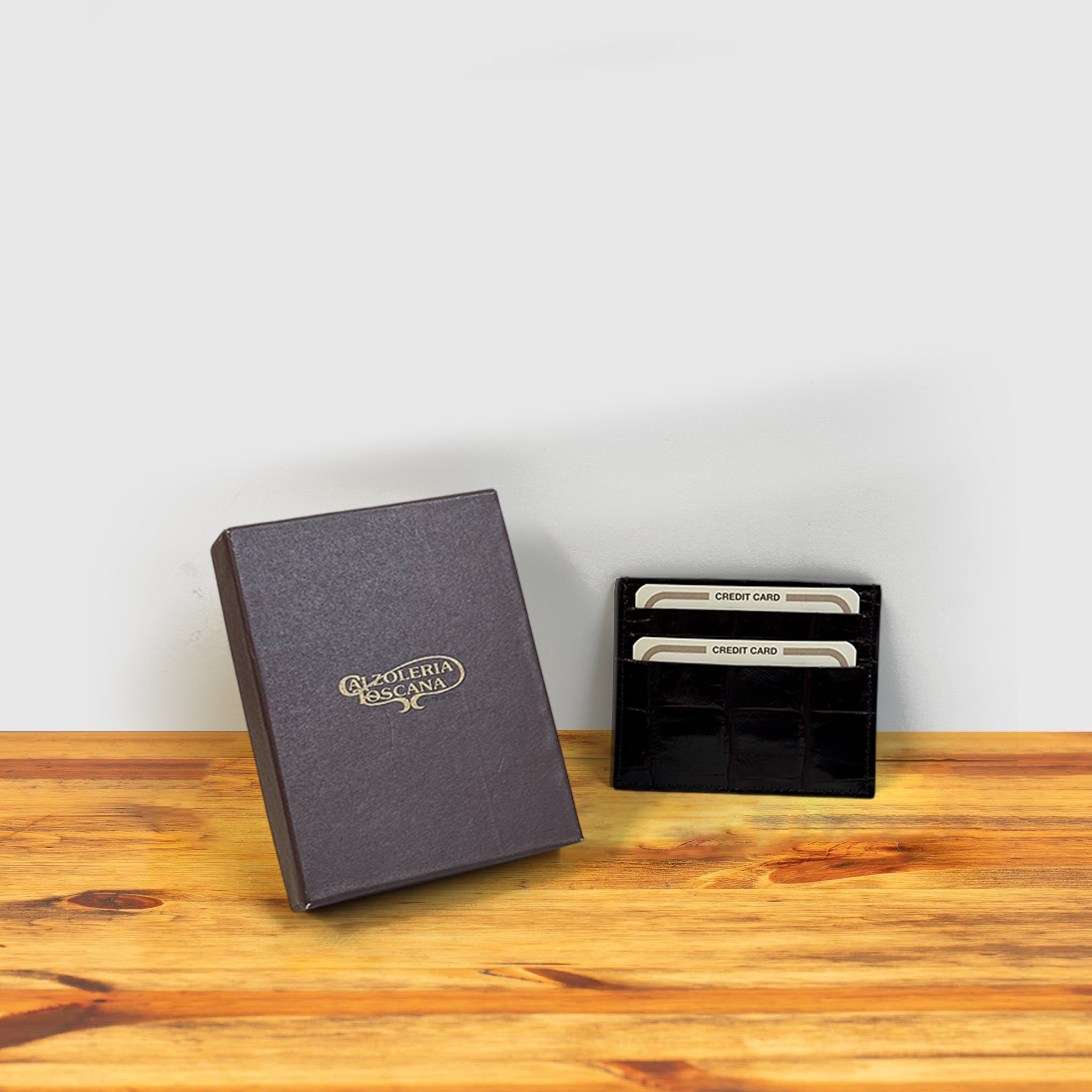 Brown crocodile-patterned cardholder with credit cards and box on a wooden surface and light gray background