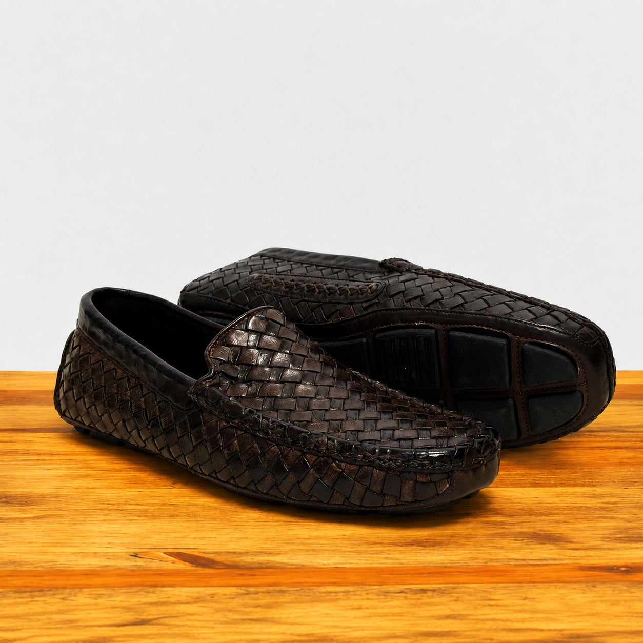 Pair of Dark Brown loafer shoe with woven pattern on a wooden surface