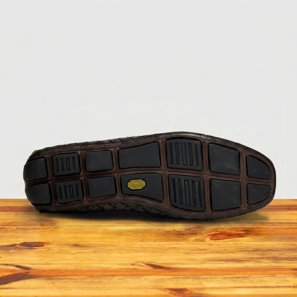 Outsole of Dark Brown shoe on a wooden surface with a light gray background