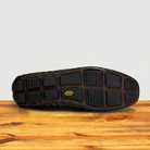 Outsole of Dark Brown shoe on a wooden surface with a light gray background