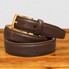 Dark brown textured leather belt coiled flat on a wooden surface, showing its gold-tone buckle and stitched edges.