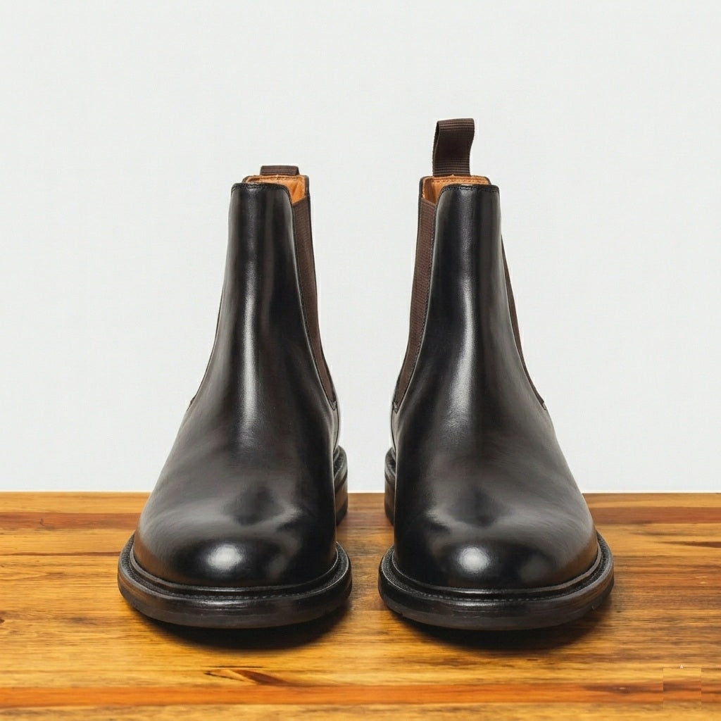 Pair of tobacco color leather boots on a wooden surface with a light gray background