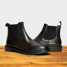 Pair of tobacco color leather Chelsea boots on a wooden surface with a light gray background