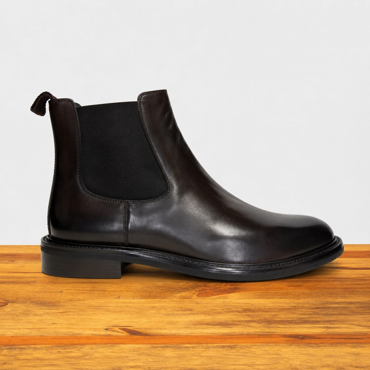 Tobacco leather Chelsea boot on a wooden surface with a light gray background