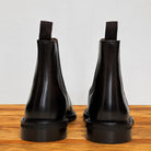 Pair of tobacco color leather boots on a wooden surface with a light gray background